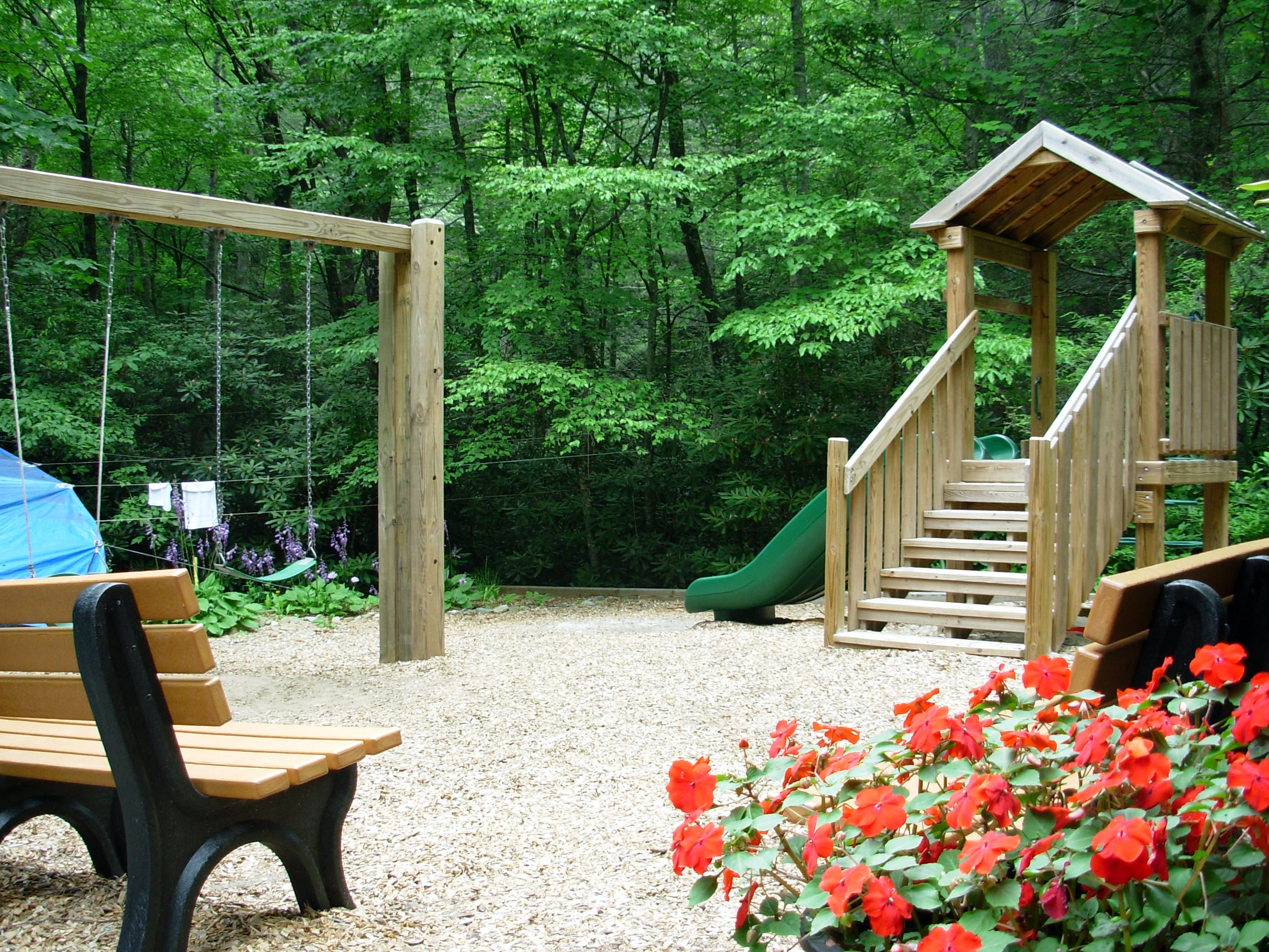 Empty Playground surrounded by trees with flower bush in the foreground.