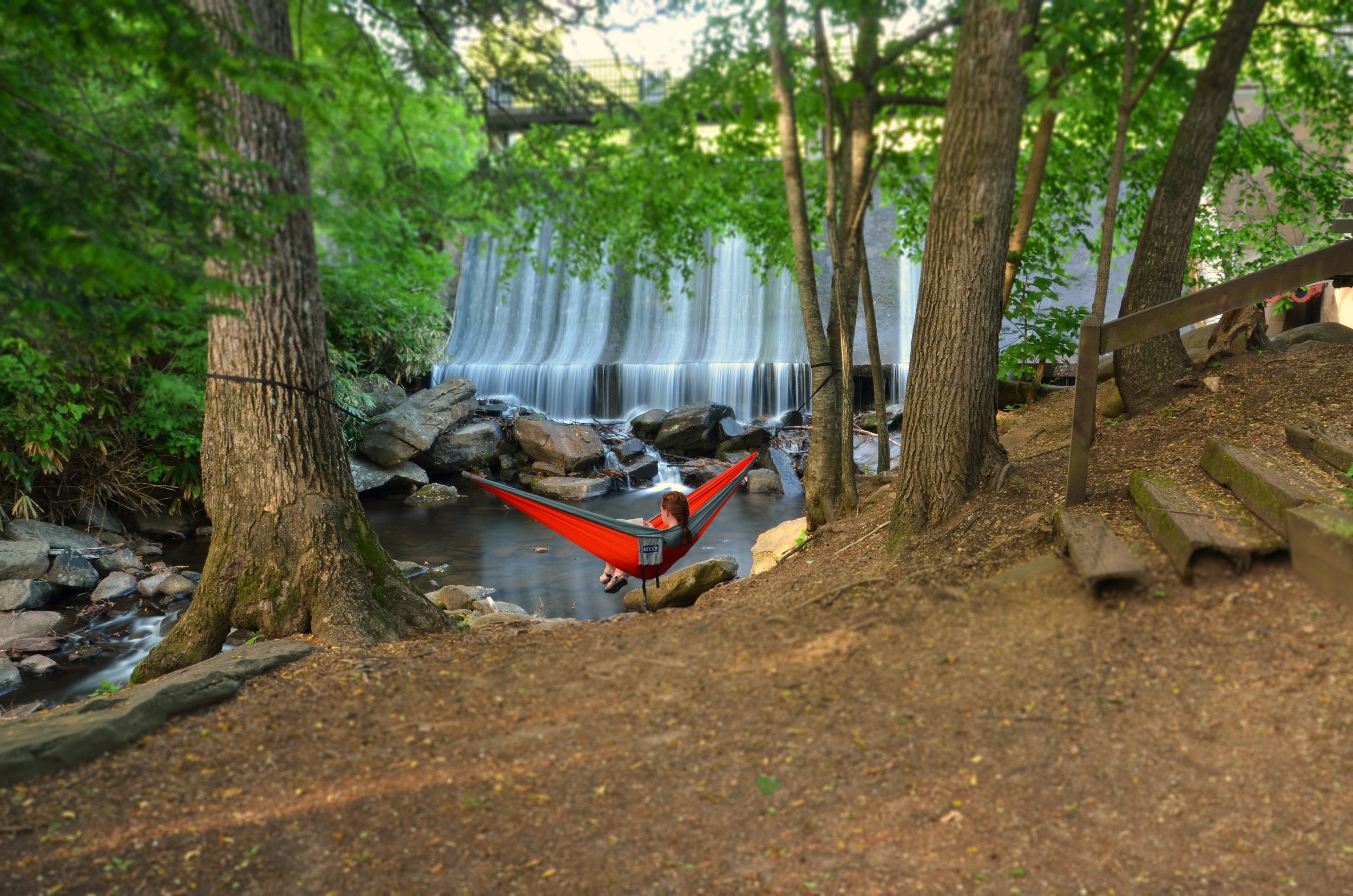 A young person relaxes in a hammock tied between two trees, overlooking the Lake Susan dam.