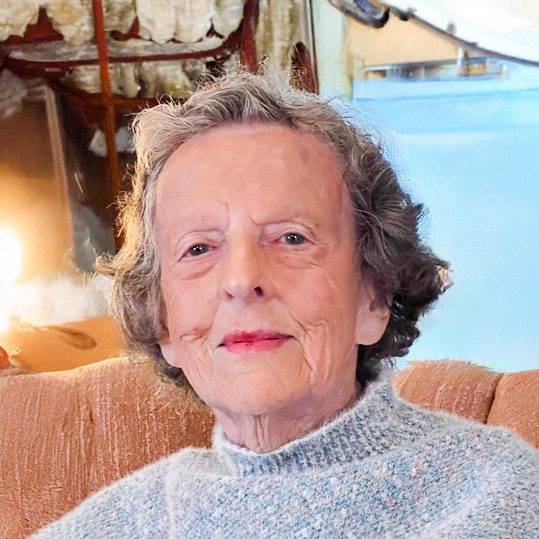Portrait of Jane Holt with grey sweater sitting in brown armchair.